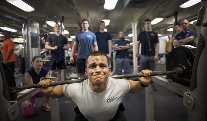How to beat gym anxiety - men crowding a man struggling to lift weights