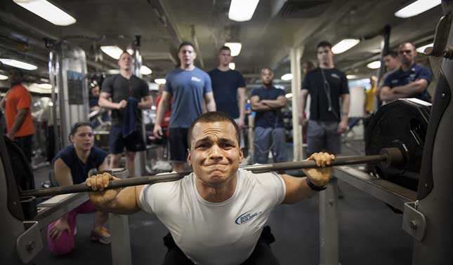 How to beat gym anxiety - men crowding a man struggling to lift weights